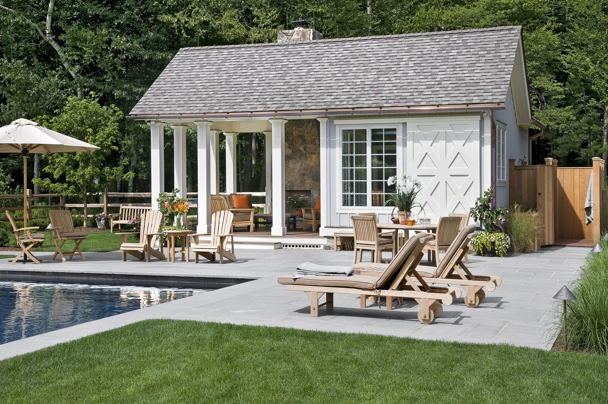 Shingled pool house with a columned terrace and teak furniture